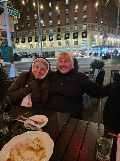Two women in winter coats at outdoor restaurant.